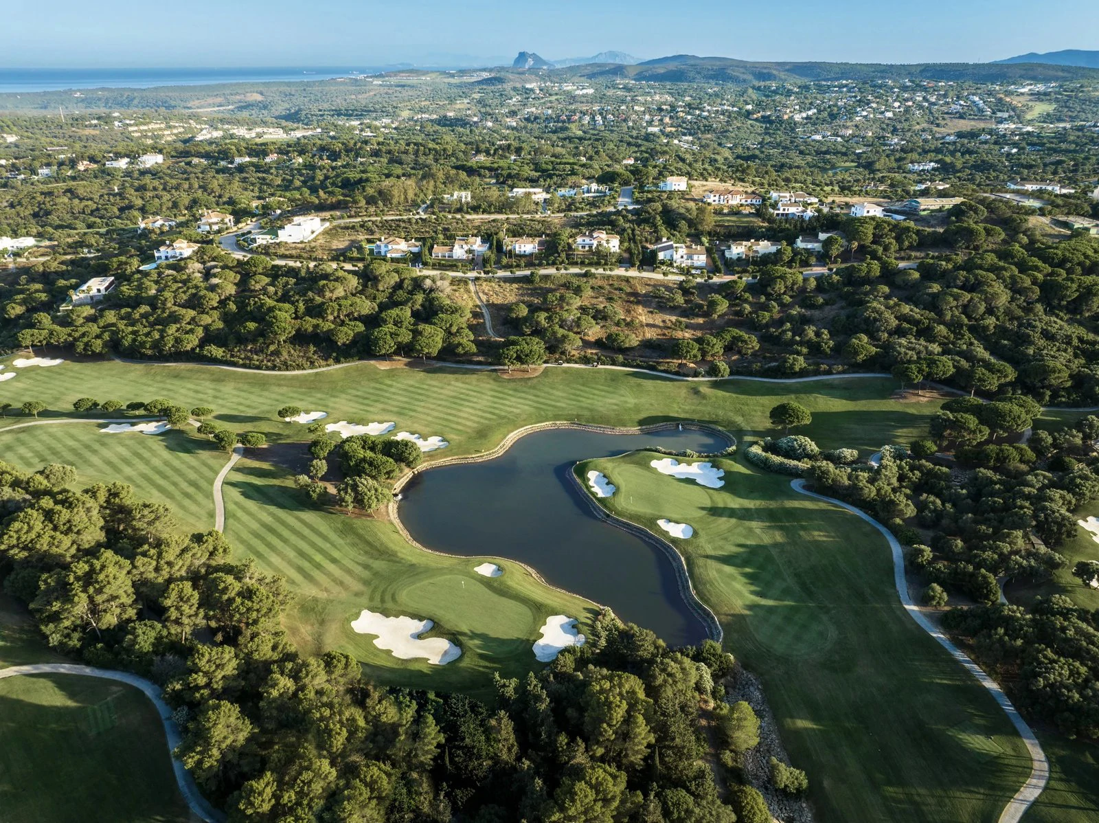 Aerial view over a golf course and lake at La Reserva, Sotogrande, with wooded hills and the Mediterranean on the horizon