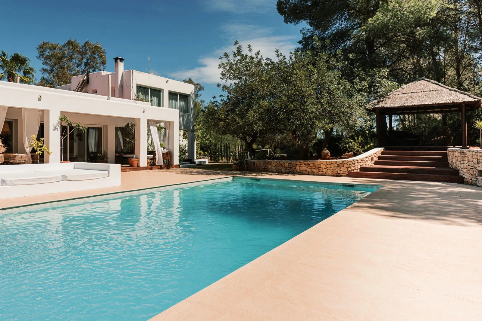 A white Ibiza villa with a large pool, sun terrace and wooden gazebo surrounded by trees